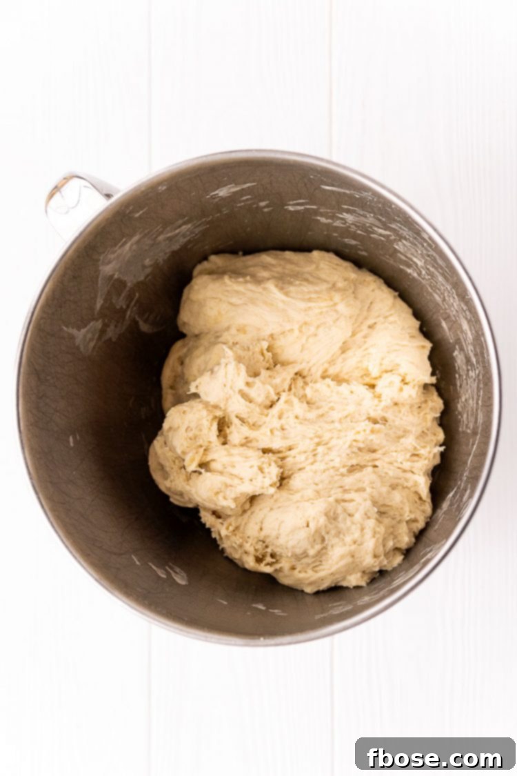 Smooth, elastic bread dough fully formed and pulling away from the sides of a stand mixer bowl, indicating proper kneading.