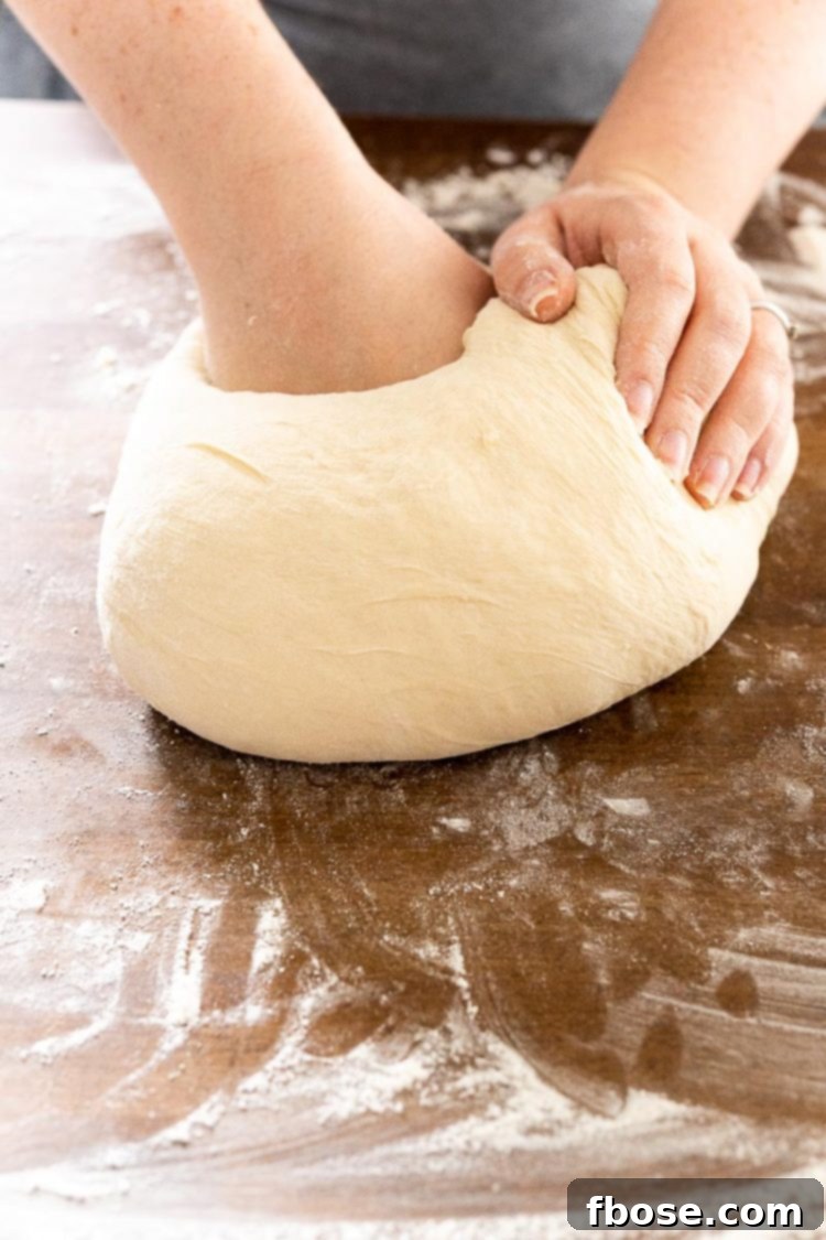 A woman's hands expertly kneading bread dough on a rustic butcher block countertop, preparing it for shaping.