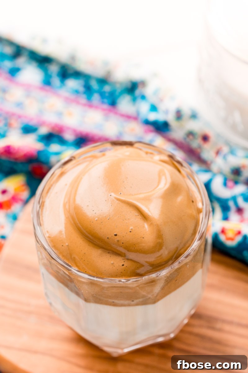 Angled overhead photo of a glass of whipped Dalgona coffee on a small cutting board.