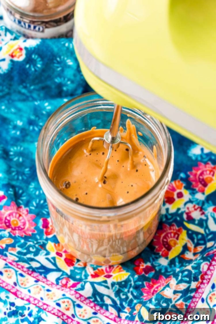 Hand mixer with one beater making whipped coffee in a mason jar.