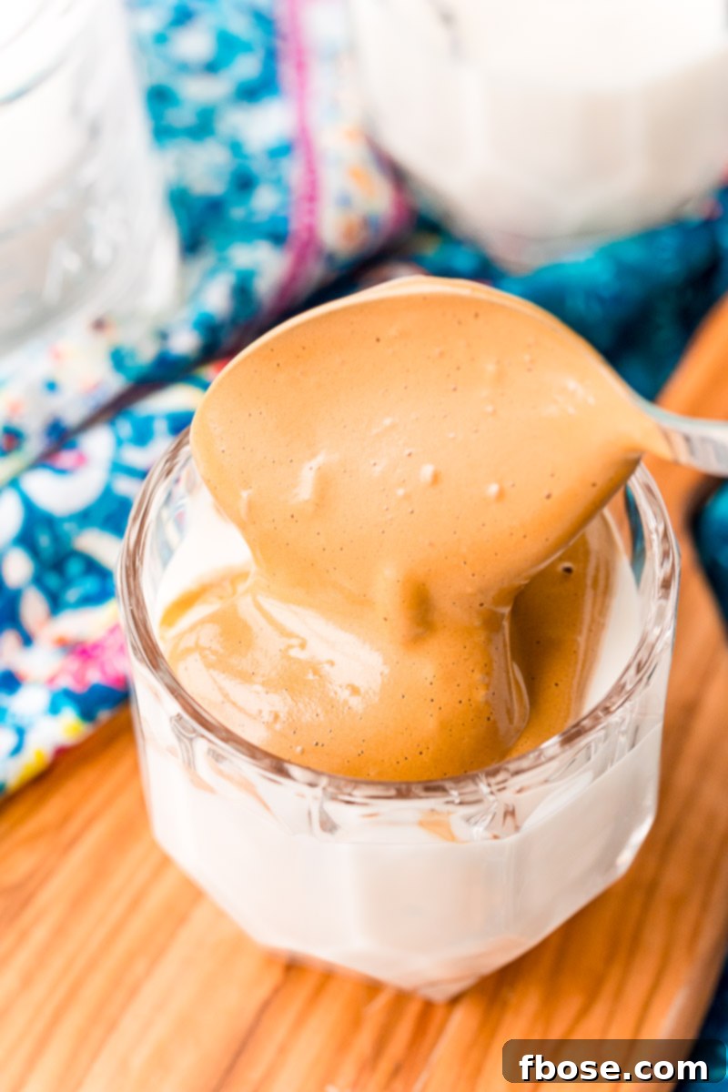 Whipped coffee being spooned over a glass of milk.