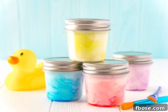 Small jars of paint stacked on top of each other with a rubber ducky and paint brushes sitting next to them on a white table.