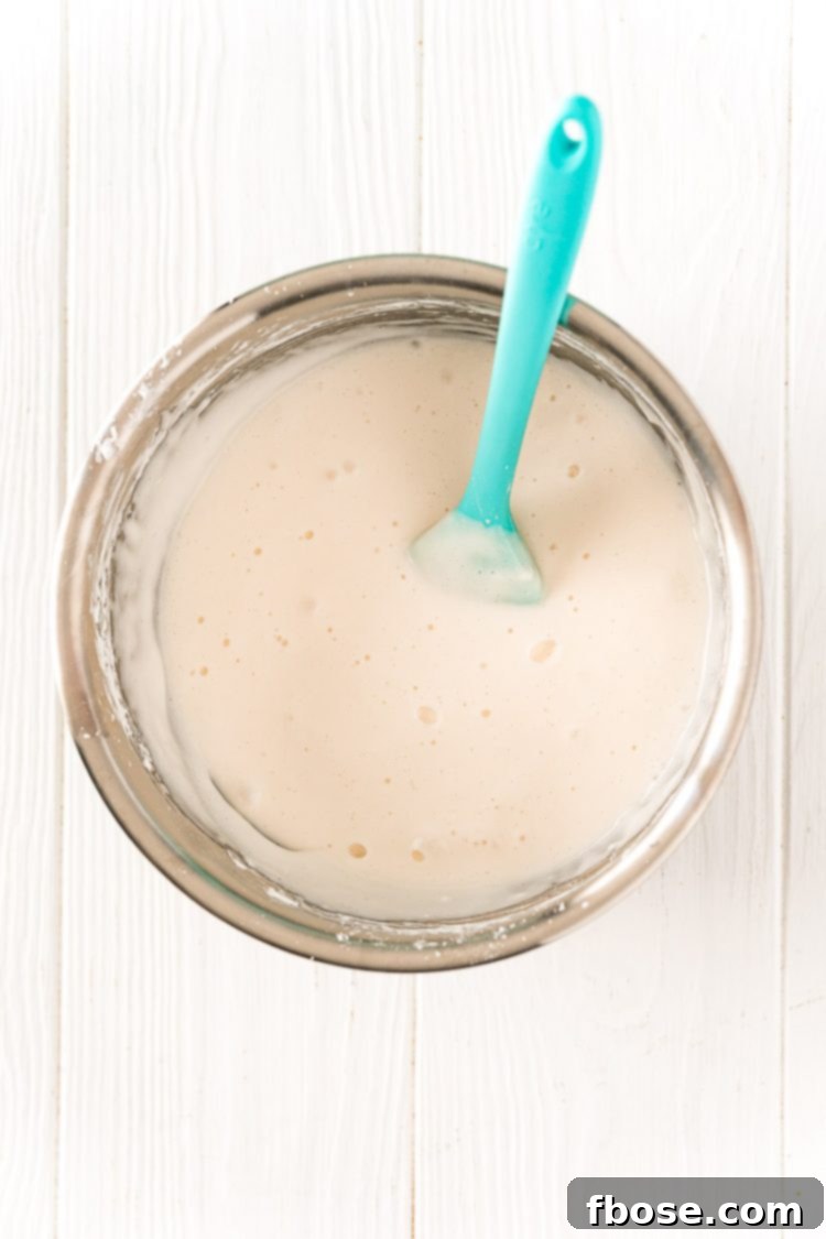 A stainless steel bowl with white bath paint being mixed with a rubber spatula.