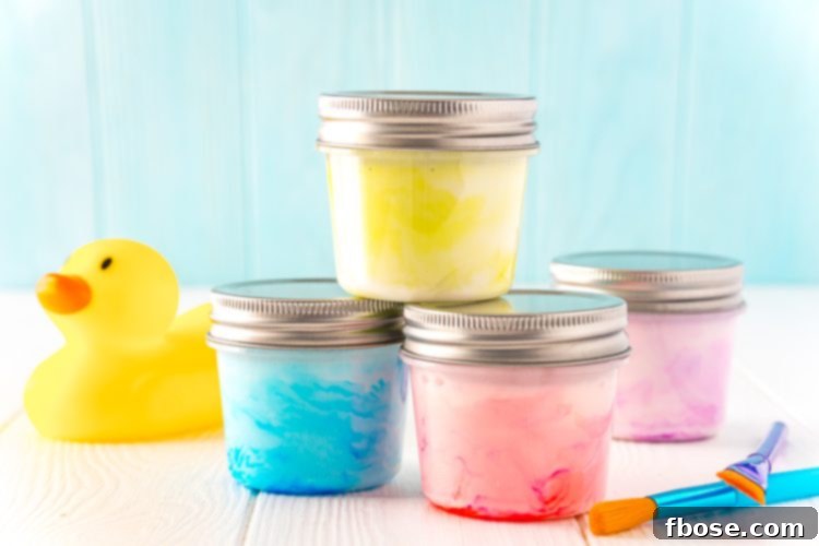 Small jars of colorful bath paint stacked on a white table next to a rubber ducky and paint brushes.