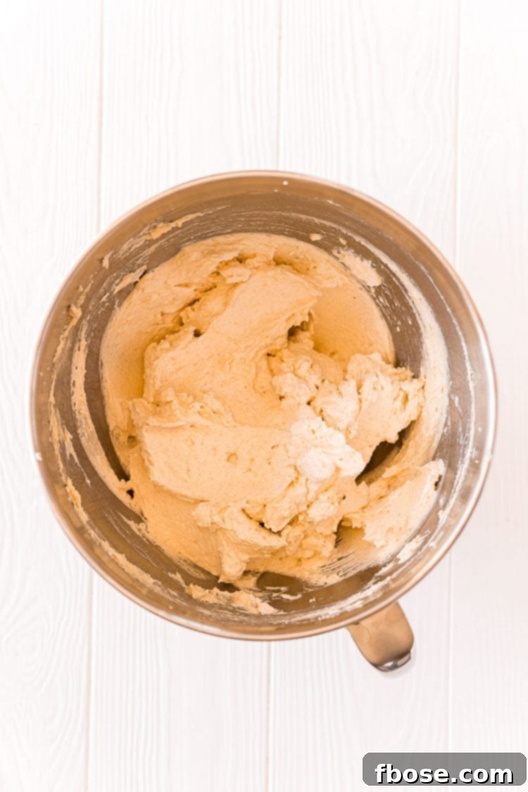 Cookie dough actively mixing in a stand mixer bowl, showing the incorporation of wet ingredients.