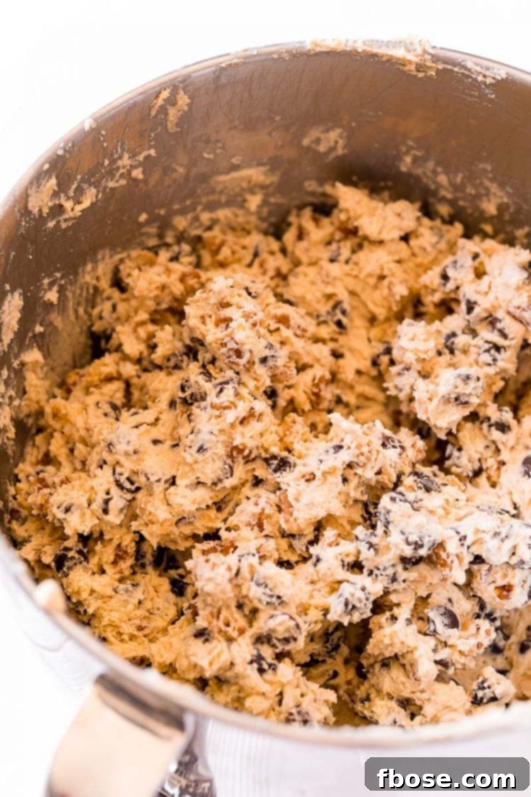 Chocolate chip cookie dough in a stand mixer bowl, ready for baking after all ingredients have been carefully folded in.