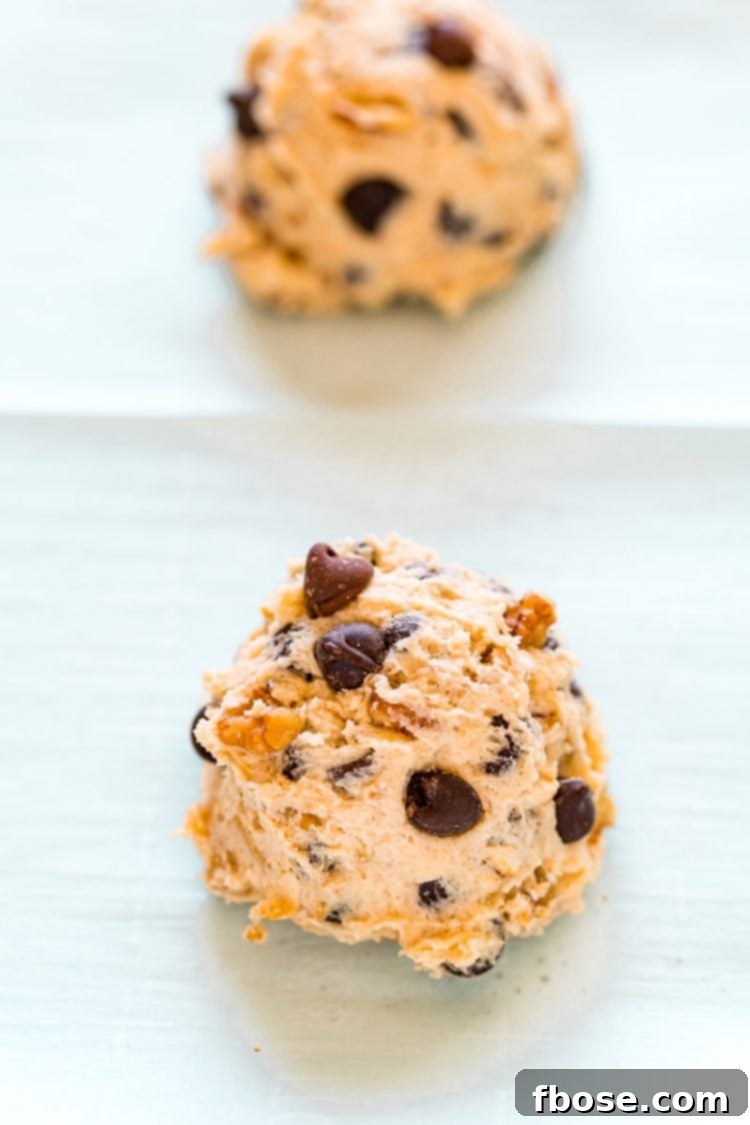 Uniform scoops of chocolate chip walnut cookie dough neatly arranged on parchment paper on a baking sheet, ready for the oven.