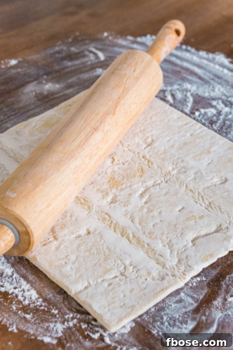 Puff pastry dough being gently rolled out on a lightly floured surface.