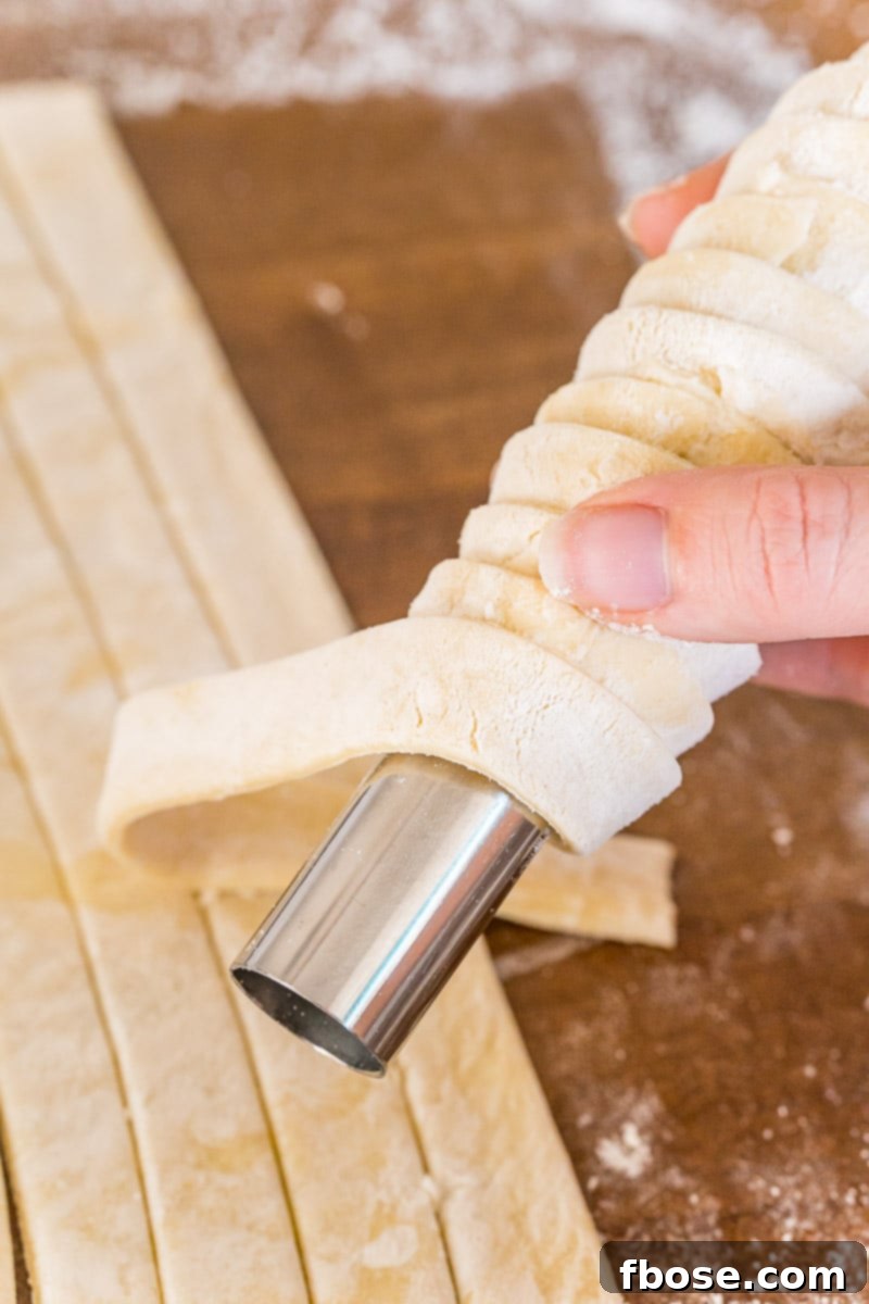 Puff pastry dough strips being carefully wrapped around a cream horn mold, with slight overlaps.