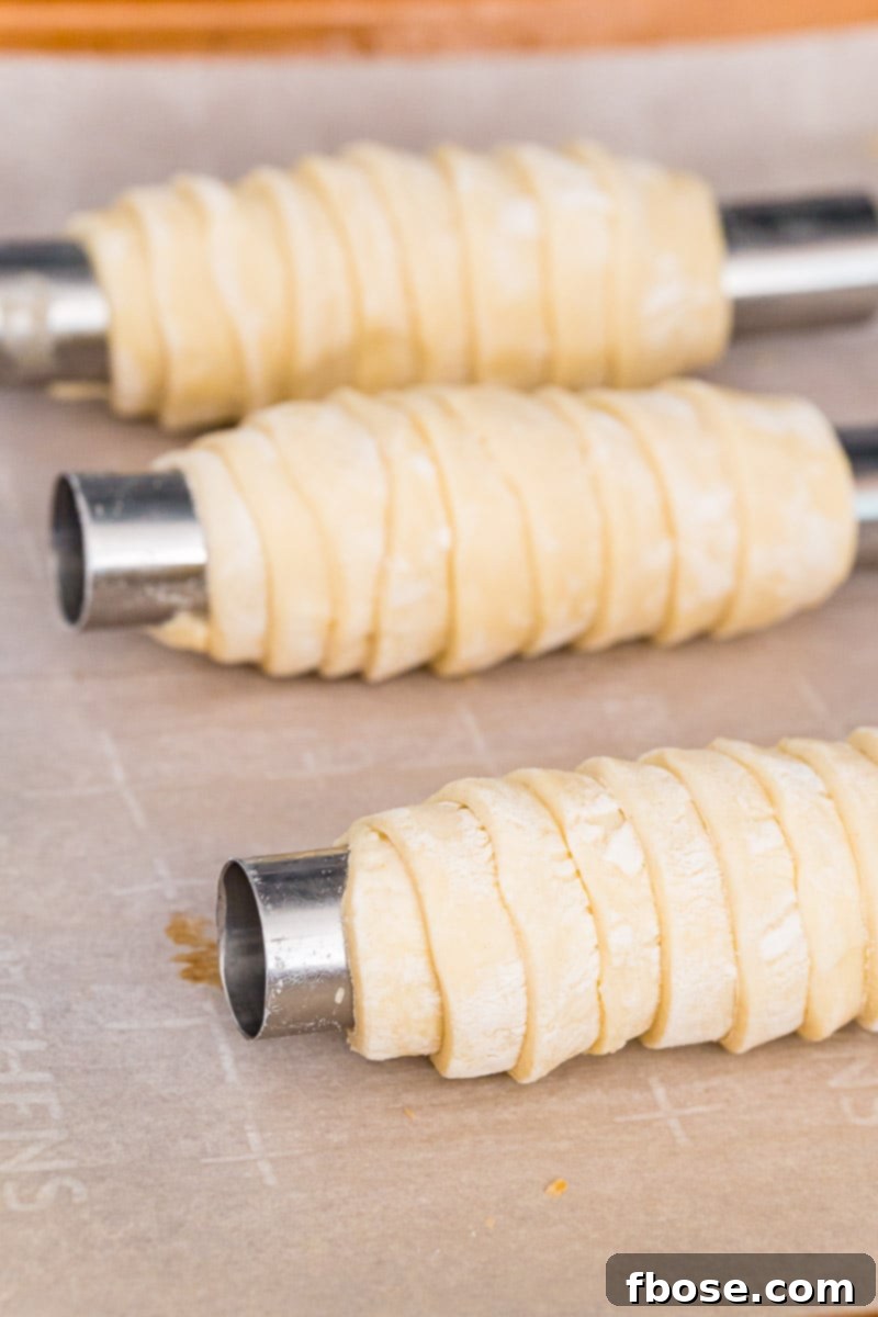 Puff pastry dough wrapped on metal molds baking on a parchment-lined baking sheet.