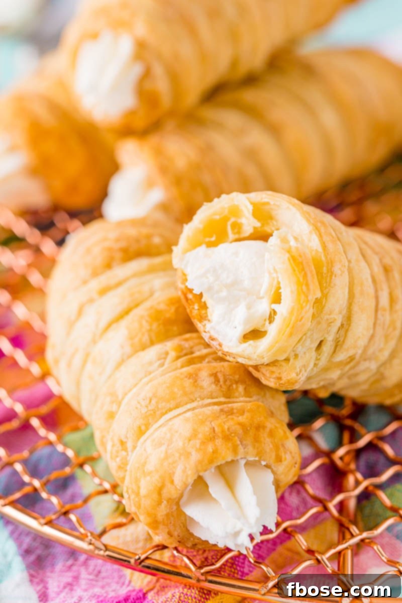 A selection of cream horns on a wire rack, one with a bite taken out, revealing the creamy interior.