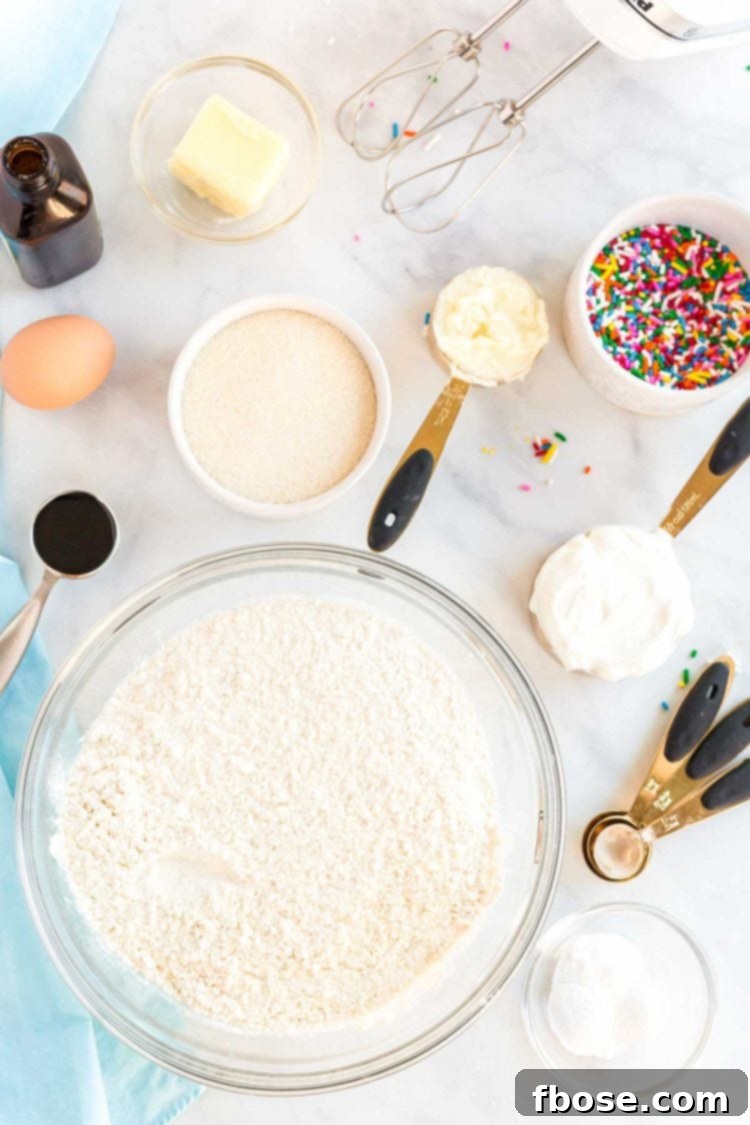 Various ingredients for making sugar cookies laid out on a white marble countertop, ready for baking.