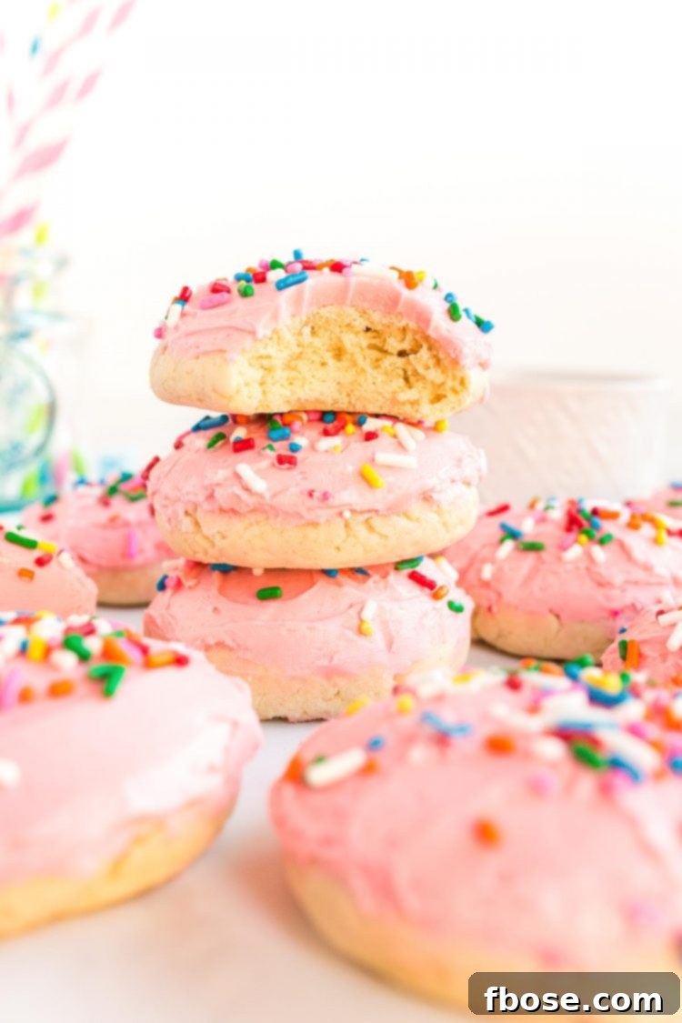 Pink frosted sugar cookies stacked on top of each other, with a bite taken out of the top cookie to reveal its soft interior.