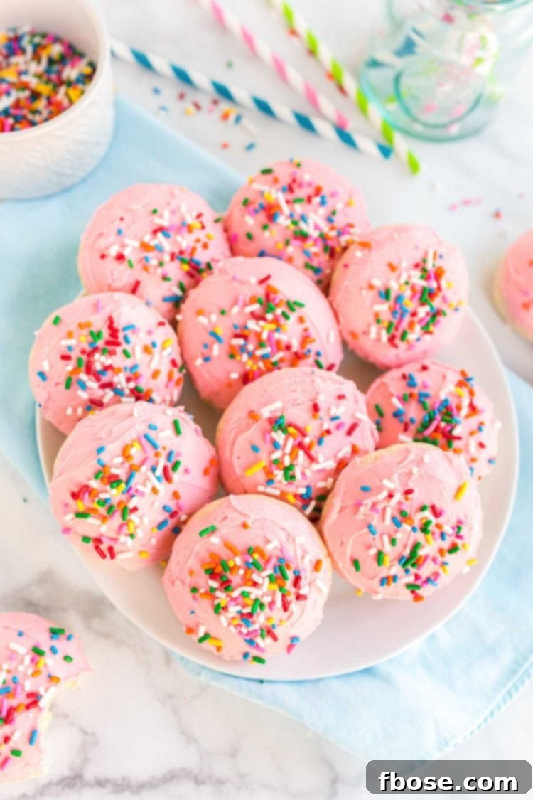 Pink frosted sugar cookies arranged on a white plate, resting on a vibrant blue napkin.