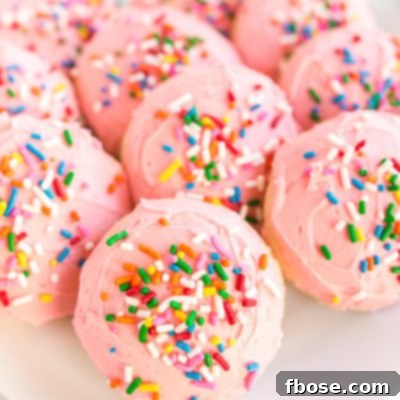 Close up photo of pink frosted sugar cookies on a plate covered in sprinkles.