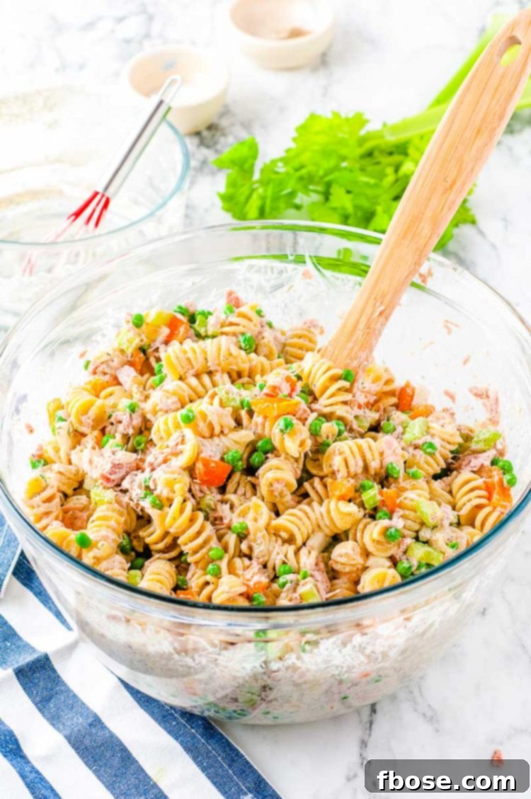 Tuna pasta salad in a large glass mixing bowl with a wooden spoon, ready to be served.