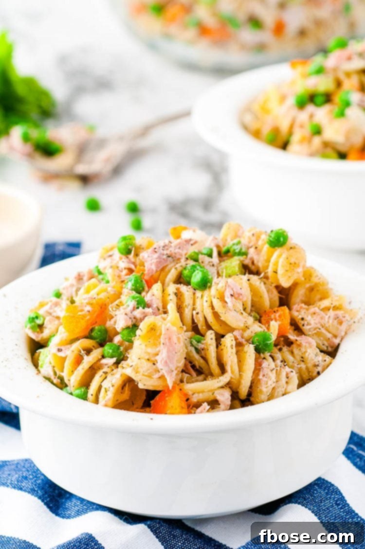 Tuna pasta salad in a small white bowl, placed on a white and blue striped napkin, ready for enjoyment.