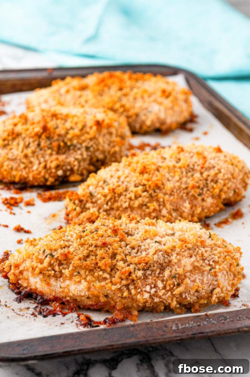 Crispy oven-baked chicken breast, golden brown and perfectly breaded, resting on a parchment-lined baking sheet.