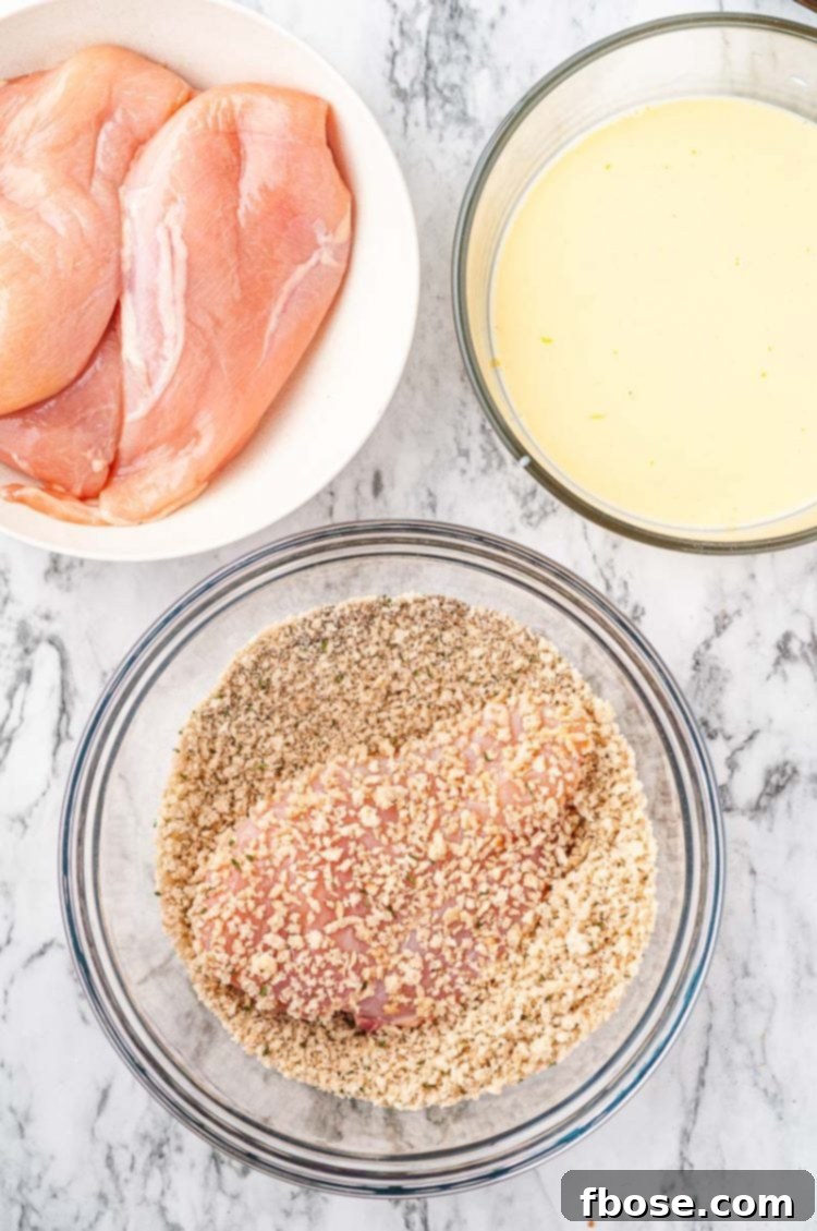 Chicken breasts being breaded in two separate prep bowls, showing the wet and dry mixture.
