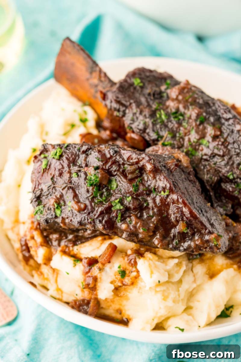 Platter of braised beef short ribs elegantly arranged over a bed of creamy mashed potatoes, garnished with fresh herbs, ready to be served.