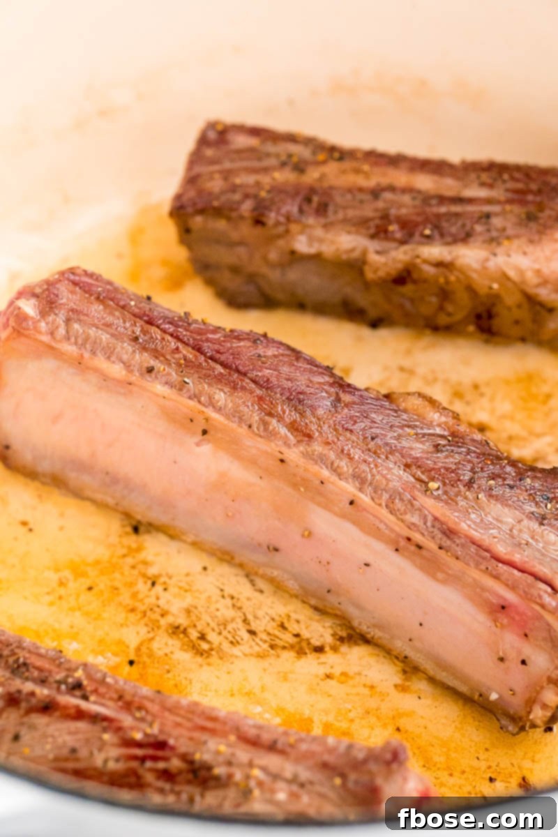 Beef short ribs actively searing to a golden brown in a Dutch oven, capturing rich flavors on all sides.