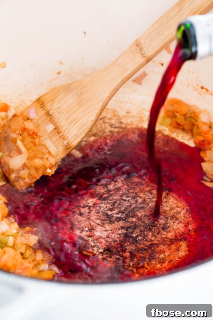 A stream of red wine being poured into a hot Dutch oven, deglazing the flavorful brown bits from the bottom of the pan.