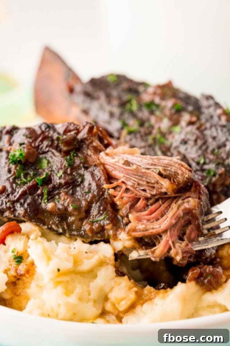A fork piercing a piece of braised beef short rib, showcasing its incredible tenderness and juicy texture, ready for a bite.