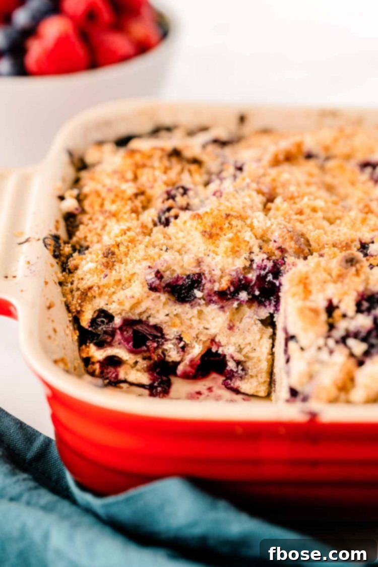 A blueberry buckle in a baking dish with one slice removed, revealing the moist interior and blueberries.