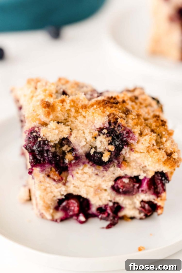 A slice of blueberry buckle on a white plate, showing the layers of cake and crumble.