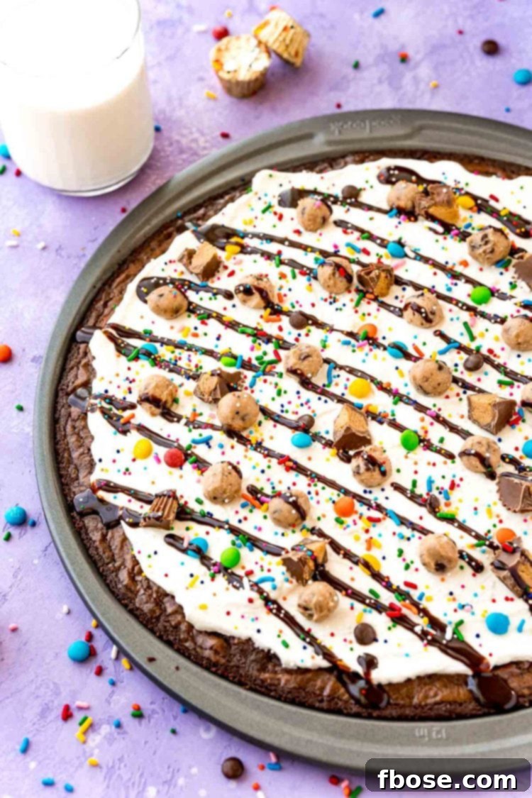 Close up photo of brownie dessert pizza in a pan on a purple surface with candy scattered around.