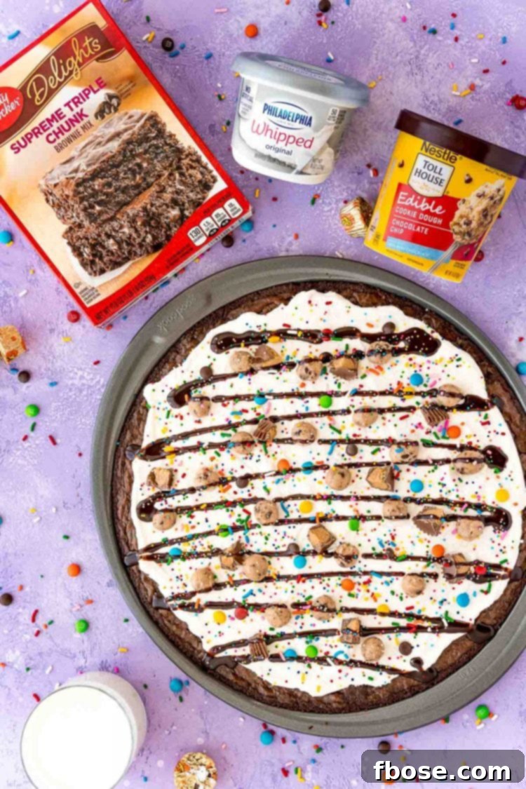 Overhead photo of brownie pizza with a box of brownie mix, container of cream cheese, and container of edible cookie dough.