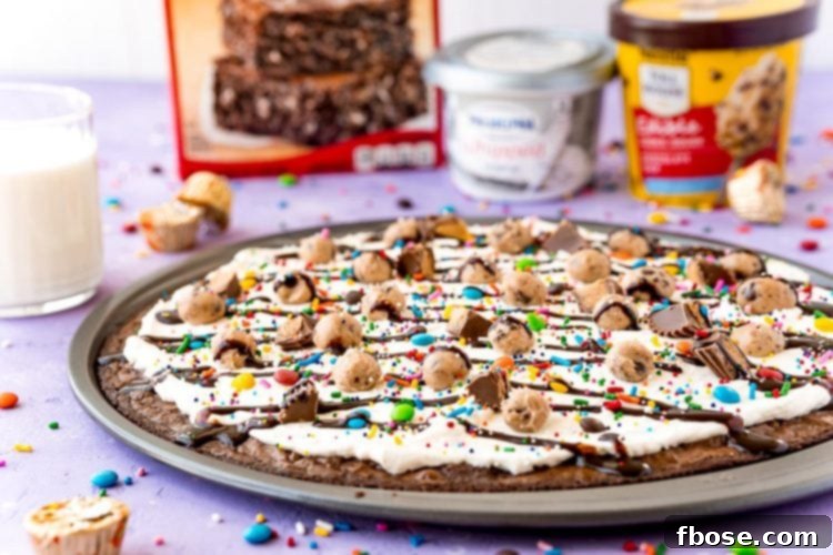 Brownie pizza on a pan with ingredients and a glass of milk in the background.