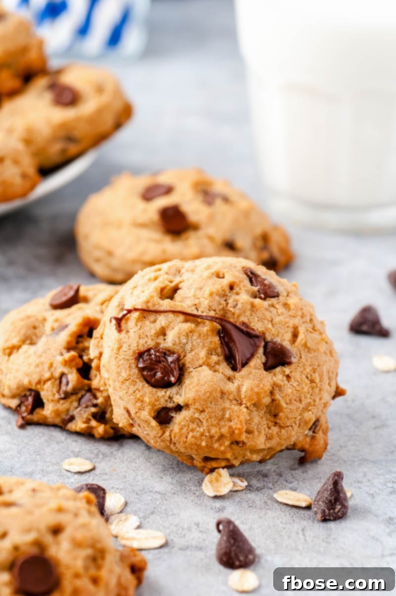 Chocolate Chip cookies on a counter with chocolate chips scattered around and a glass of milk in the background.