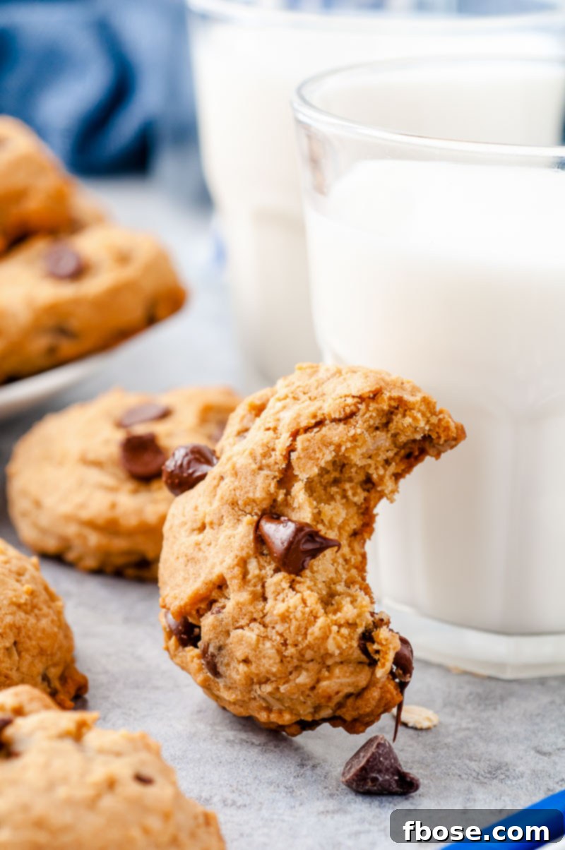 Oatmeal chocolate chip cookie with a bite taken out of it leaning against a glass of milk.