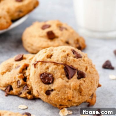 Chocolate Chip cookies on a counter with chocolate chips scattered around and a glass of milk in the background.