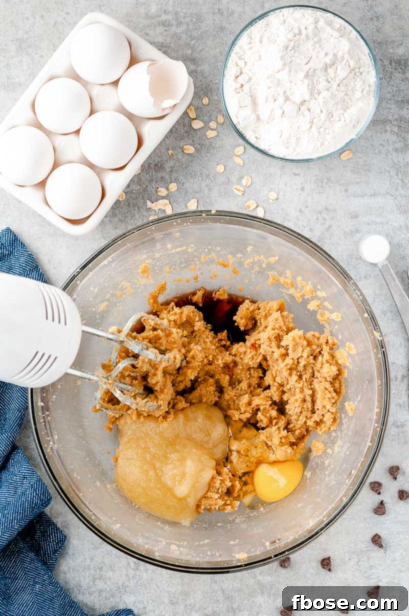Ingredients being blended to make oatmeal chocolate chip cookies in a large glass bowl.