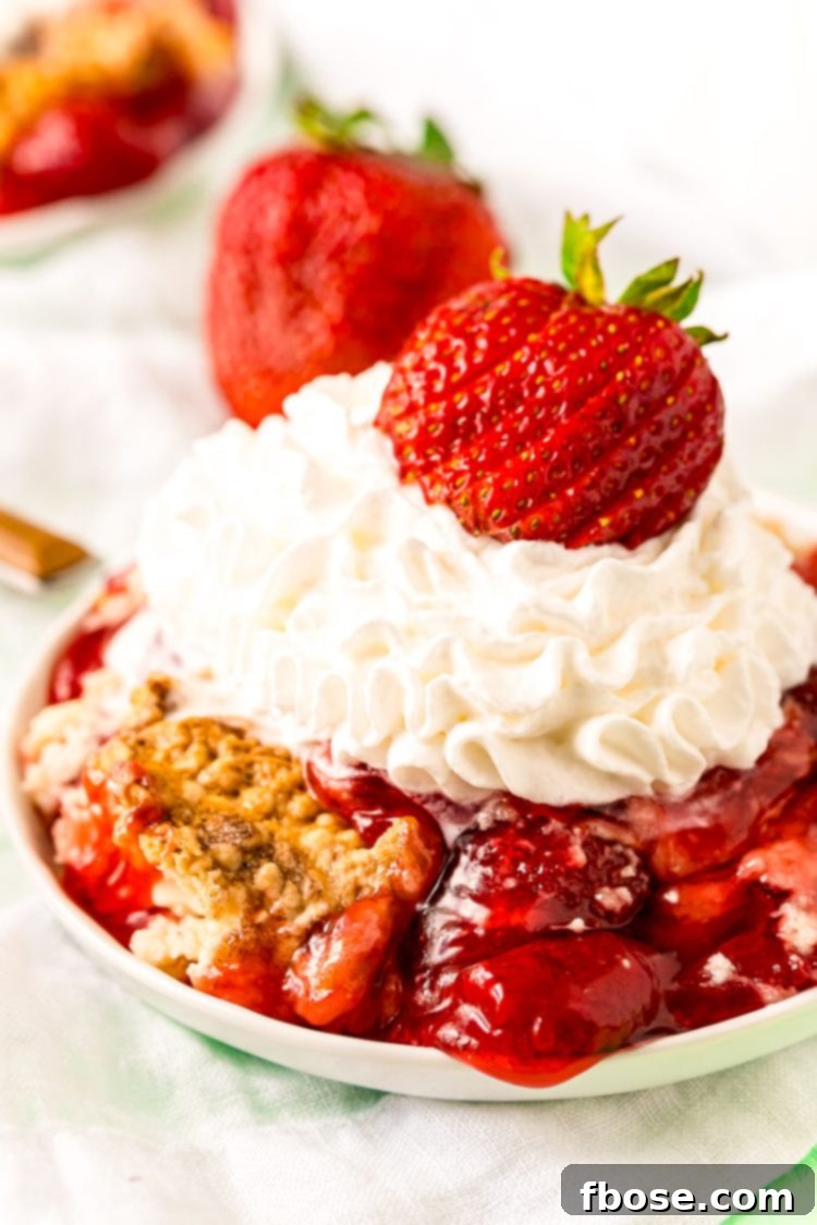 A slice of Strawberry Dump Cake on a white plate, elegantly topped with whipped cream and a fresh strawberry garnish, showcasing its golden-brown crust and vibrant fruit filling.