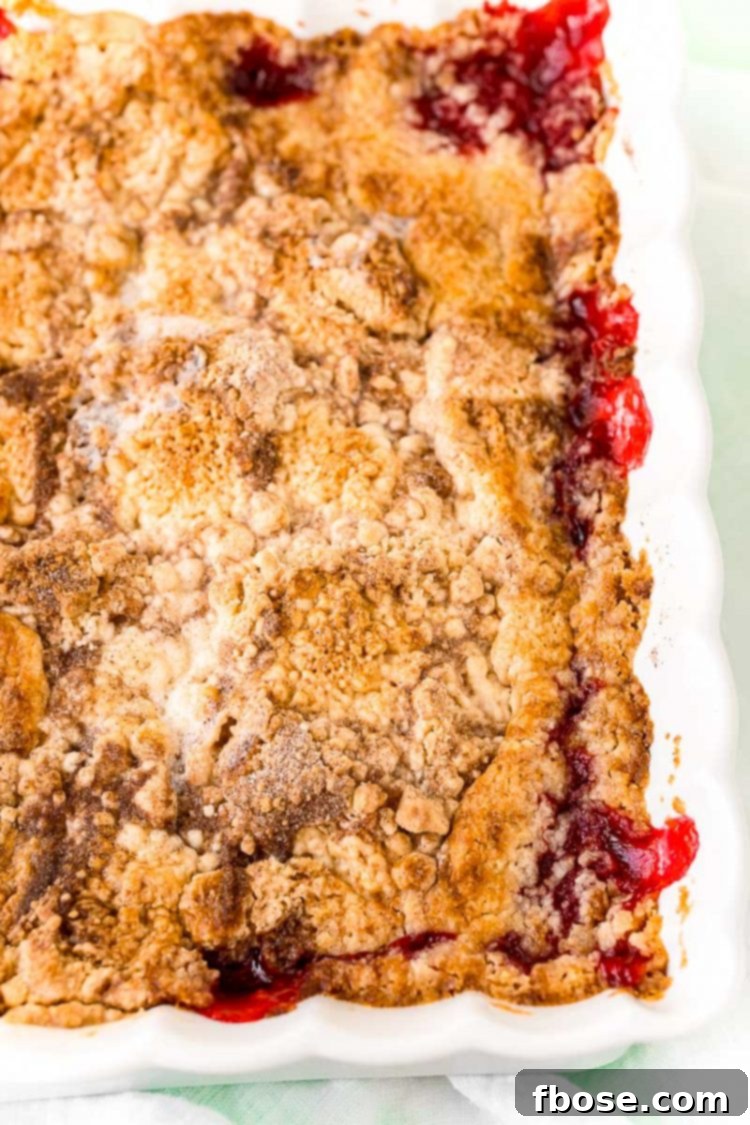 A close-up view of strawberry dump cake cobbler in a white ceramic baking dish, showing the bubbly fruit filling and the golden, crumbly cake topping, ready to be served.