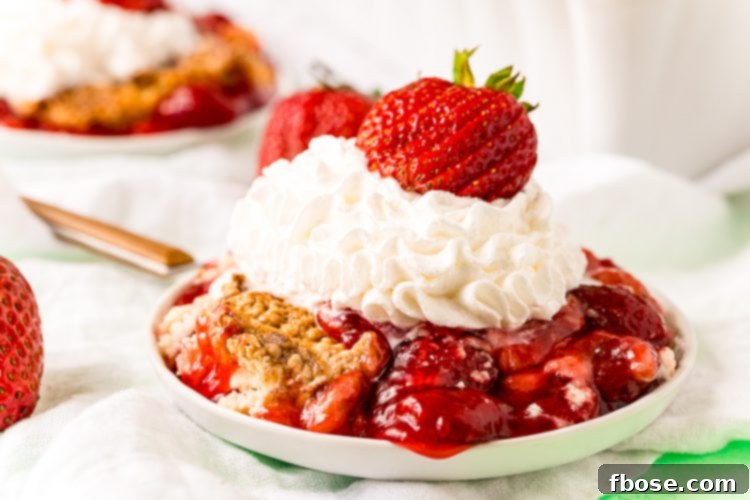 A close-up photo of strawberry cobbler on a white plate, beautifully garnished with whipped cream and a fresh strawberry, highlighting its inviting texture and vibrant color.