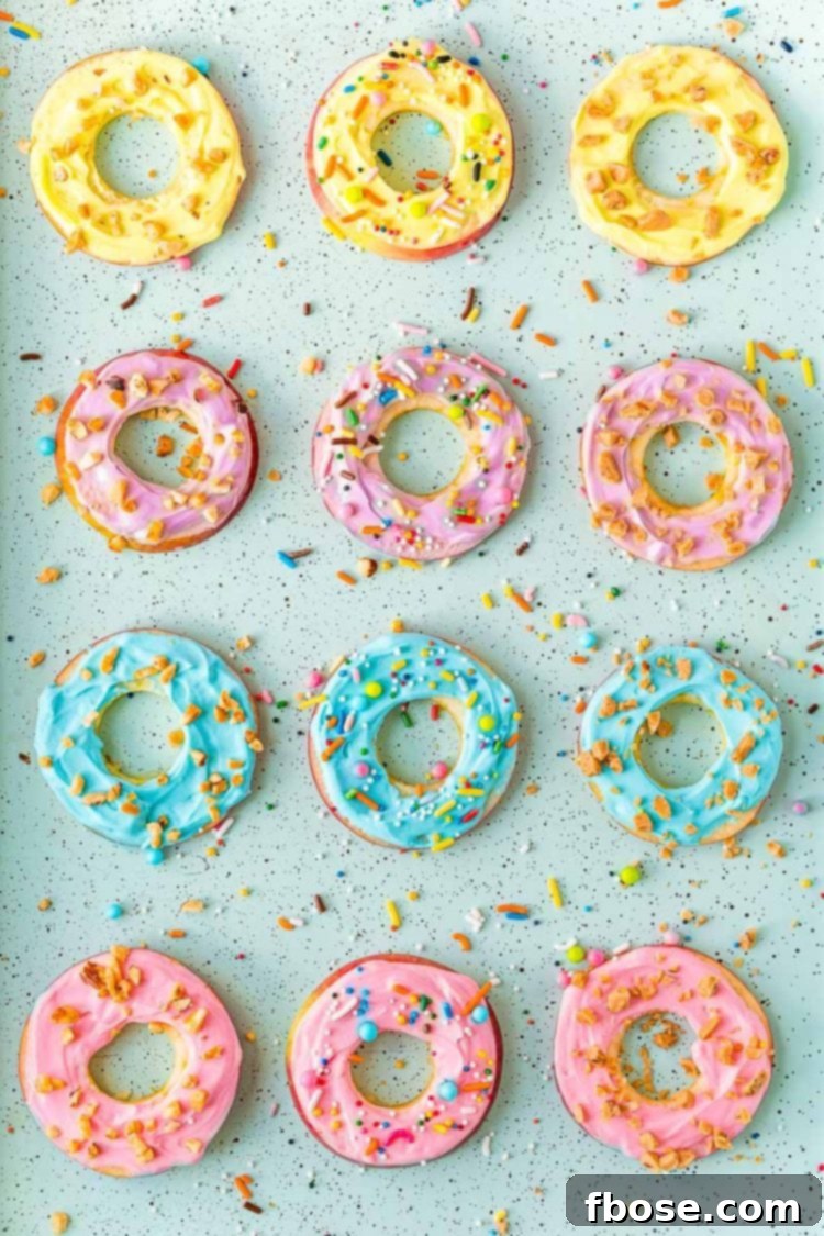 Overhead photo of apple slices with colorful frosting on them on a blue baking sheet with sprinkles, emphasizing their vibrant and healthy appeal.