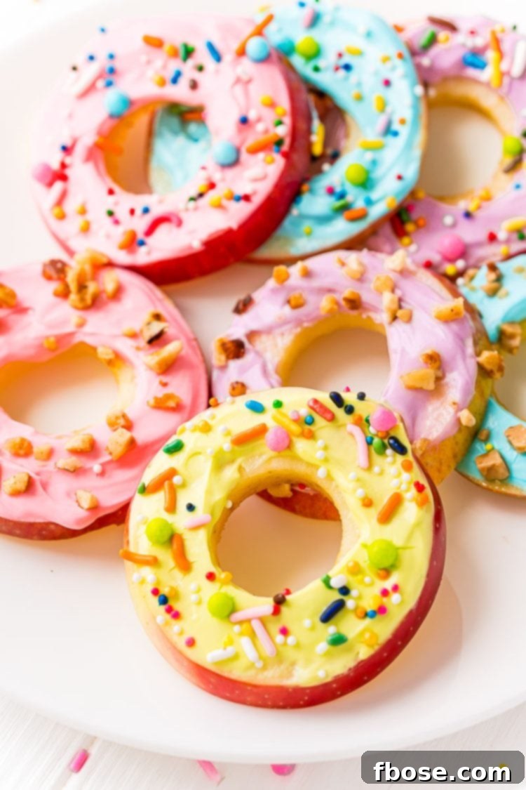 Close-up of beautifully decorated apple donut slices topped with cream cheese frosting and colorful sprinkles on a pristine white plate, showcasing their inviting texture.