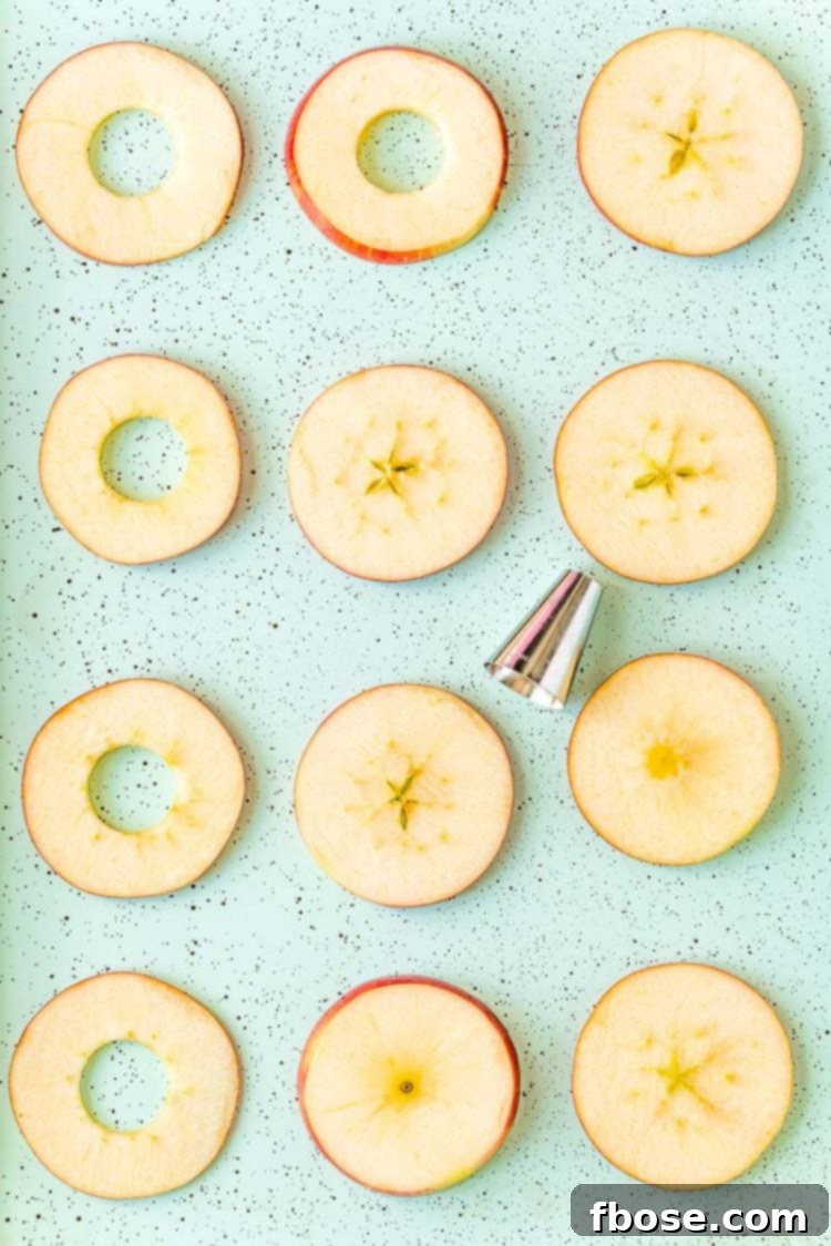 Detailed shot of round apple slices laid out on a blue baking sheet, in the process of being cored using a precise round piping tip.