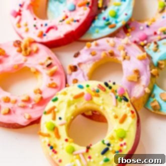 Apple donut slices topped with cream cheese frosting and sprinkles on a white plate.