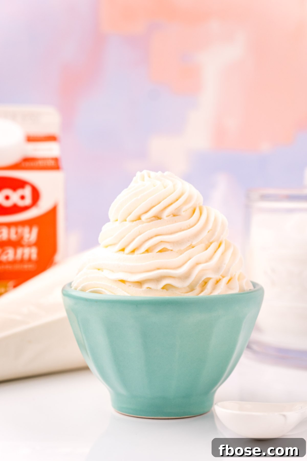 A small light blue bowl filled with piped whipped cream with a bag of whipped cream and a carton of heavy cream in the background.