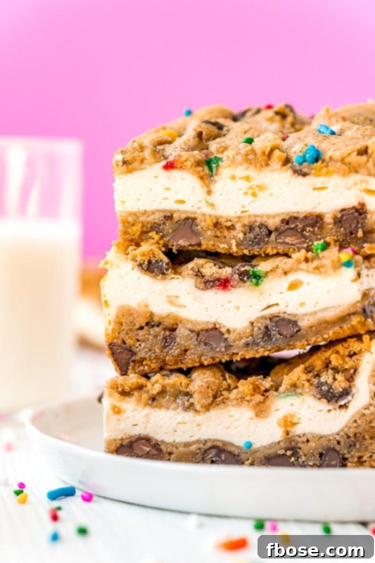 Close up photo of a stack of golden brown chocolate chip cookie cheesecake bars on a white plate with colorful sprinkles scattered on the table, highlighting the distinct cookie and cheesecake layers.