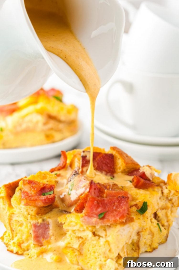 Rich, golden Hollandaise sauce being generously poured over a serving of Eggs Benedict Casserole on a plate, enhancing its appeal.