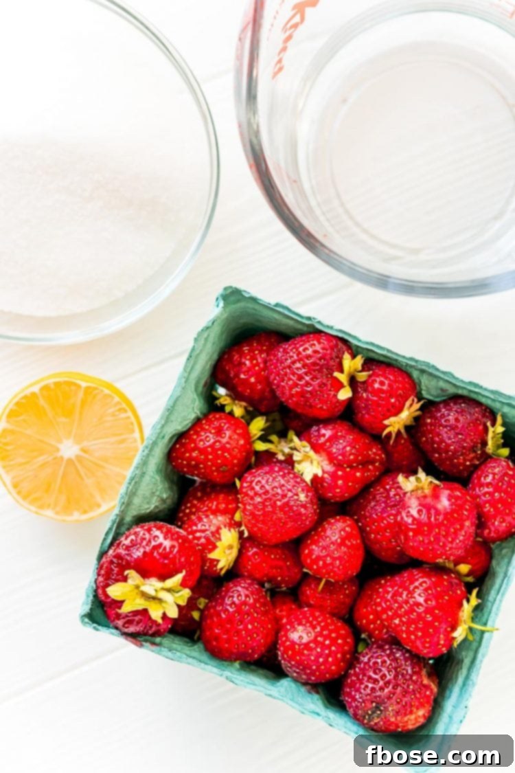 Ingredients to make strawberry simple syrup laid out on a clean white table, emphasizing freshness.