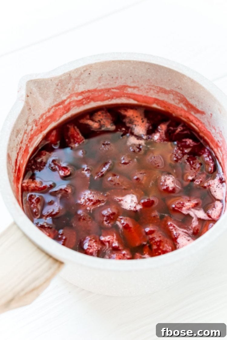 Boiled strawberries in a small pot, having released their color and flavor into the syrup.
