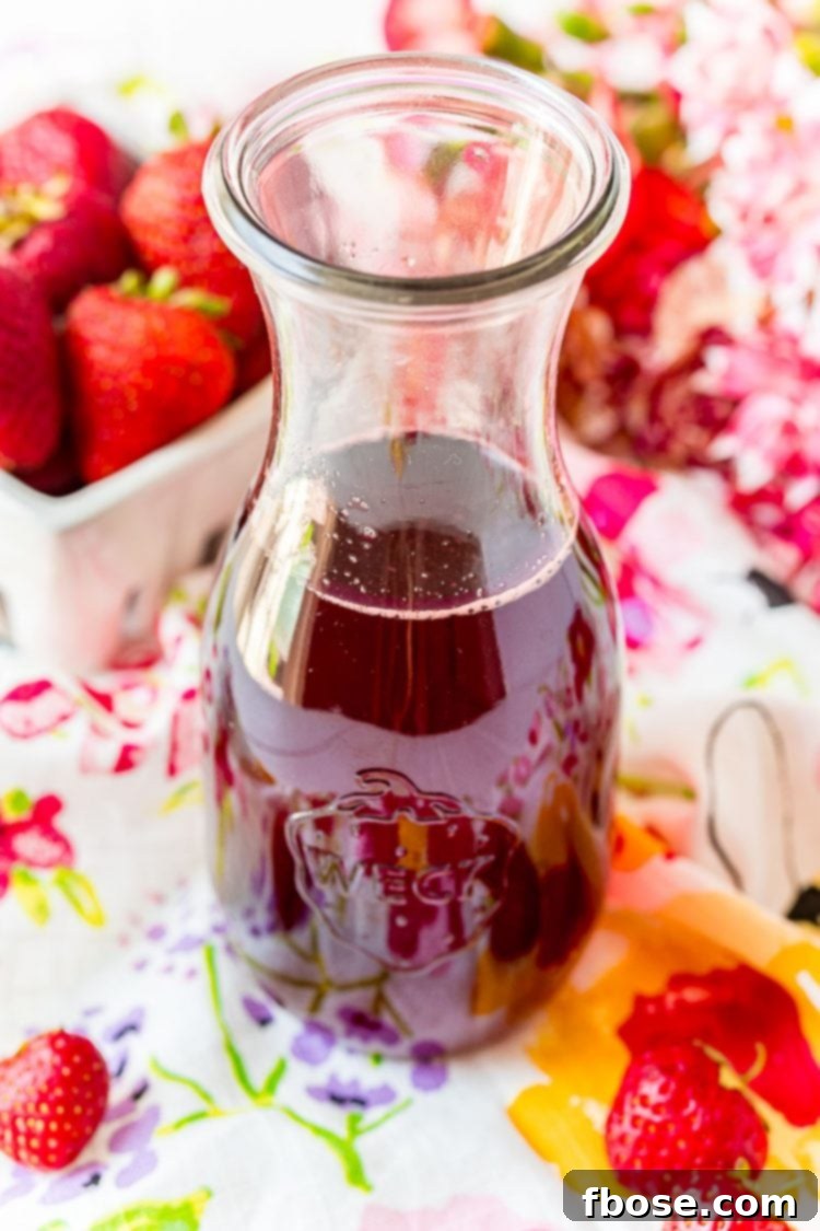A glass carafe filled with strawberry simple syrup, placed on a colorful napkin, showcasing its appeal.