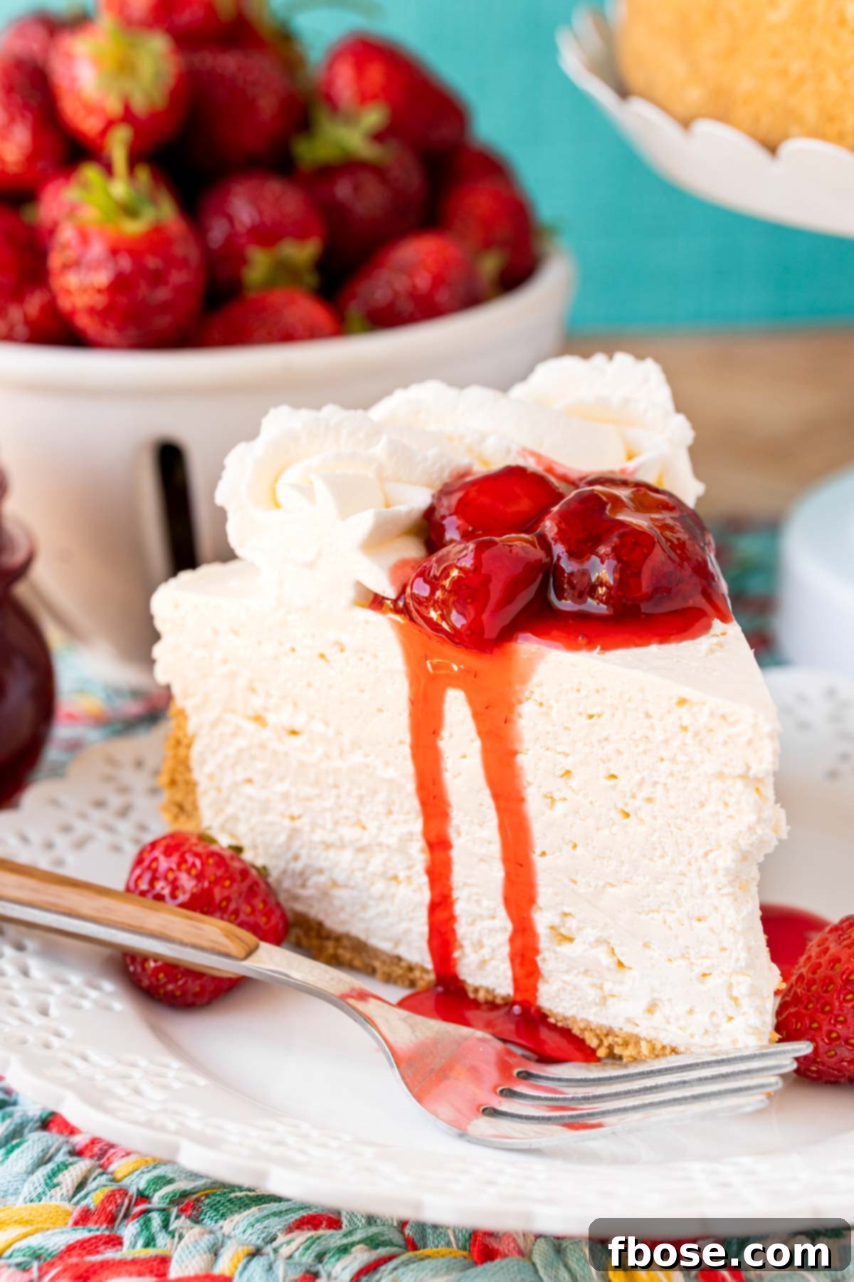 A slice of no bake cheesecake on a white plate topped with strawberry sauce and served with a fork.